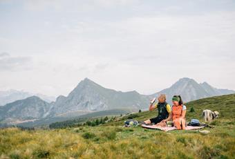 Mann und Frau im Sommer auf einer Almwiese auf Picknickdecke mit Hintergrund Berg Ifinger in Hafling in Südtirol.